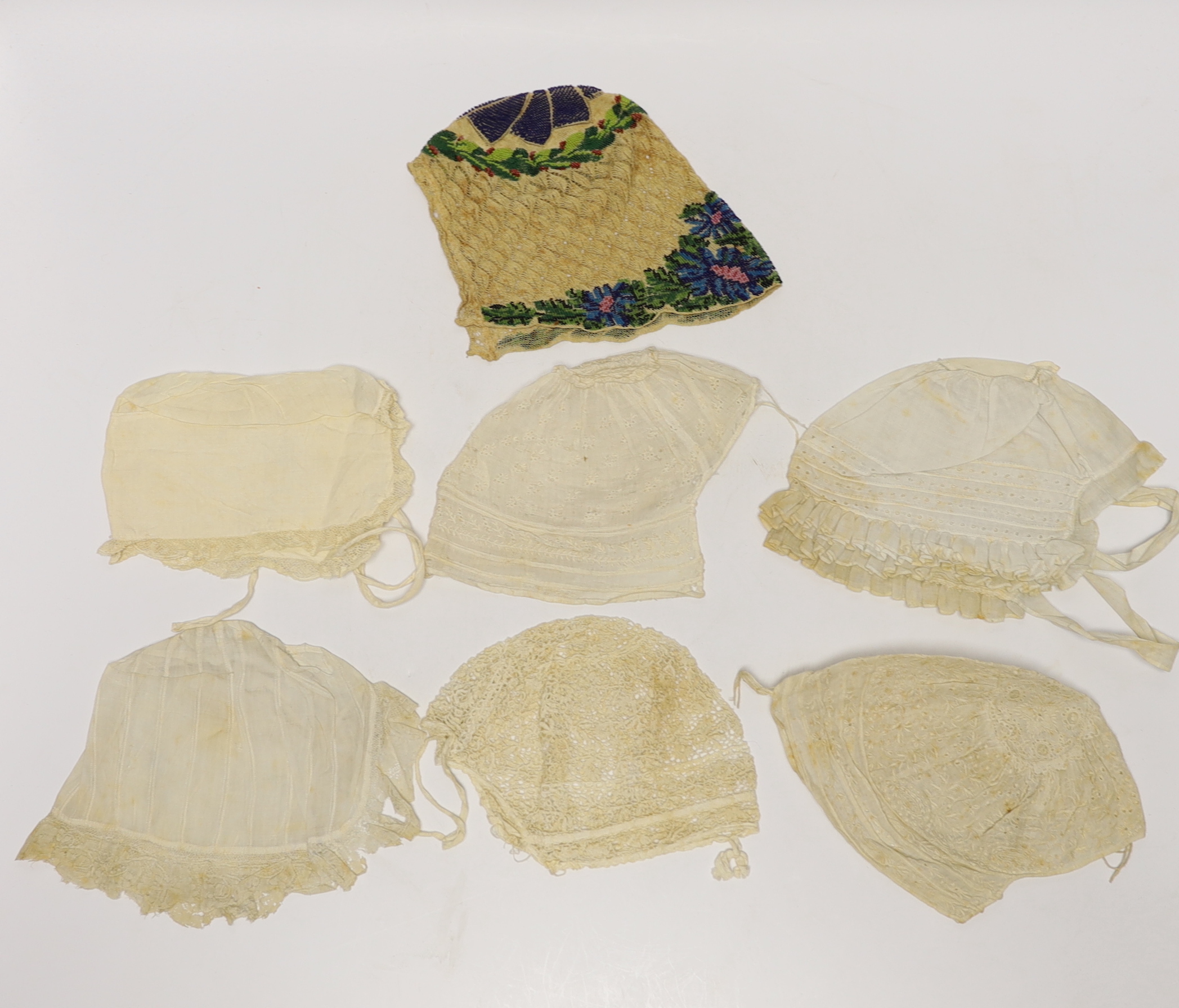 Seven baby bonnets, late 18th / 19th century, including a fine bobbin lace bonnet and unusual silk knitted and multi coloured floral designed beaded bonnet